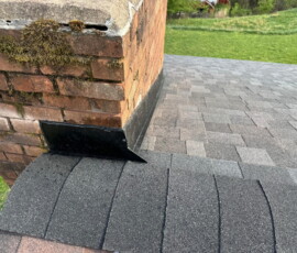 Close-up of a brick chimney with metal flashing and asphalt shingles on a residential roof.