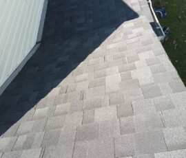 Close-up view of a newly installed asphalt shingle roof next to white siding, with a truck visible in the background.